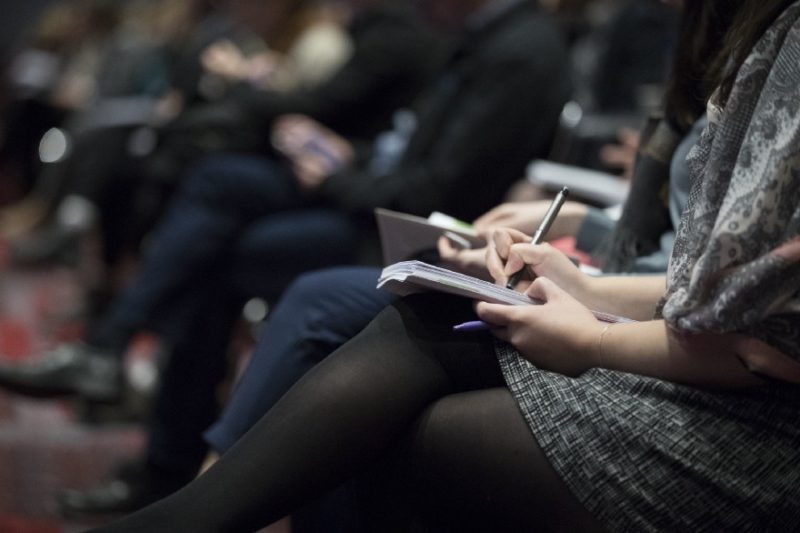 Mid-level view of people taking notes on paper in a meeting room.